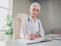 Lekarka w białym kitlu z niebieskim stetoskopem pisze w notatniku. Pytanie o wypalenie zawodowe L4 kto wystawia, może być skierowane do niej.